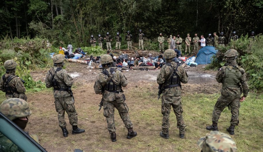 Grupa żołnierzy stojąca naprzeciw grupy migrantów.