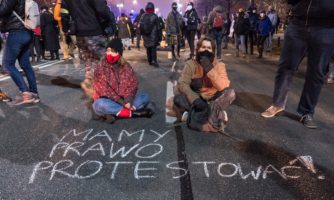 2 młode osoby siedzą na drodze przed napisanym kredą zdaniem: Mamy prawo protestować, Warszawa 9 grudnia 2020.