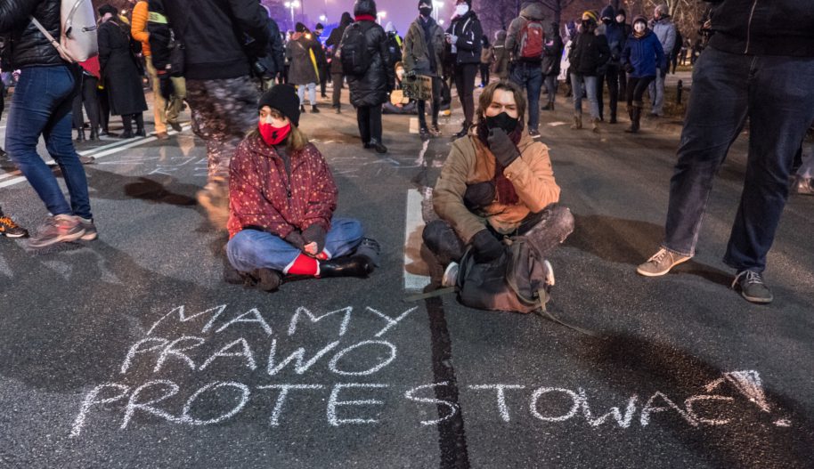 2 młode osoby siedzą na drodze przed napisanym kredą zdaniem: Mamy prawo protestować, Warszawa 9 grudnia 2020.
