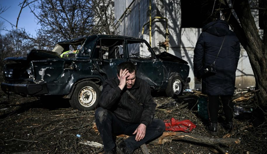 A man sits outside his destroyed building after airstrikes on the Eastern Ukraine town of Chuguiv on February 24, 2022. Photo by ARIS MESSINIS/AFP via Getty Images)