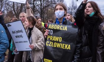 Zdjęcie z demonstracji strajku kobiet pod hasłem "Ani jednej więcej. Grupa młodych kobiet, jedna z nich trzyma baner z logiem Amnesty International i hasłem: Aborcja to prawo człowieka". Warszawa, 6 listopada 2022.