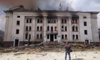 Zdjęcie frontu palącego się budynku Teatru Dramatycznego w Mariupolu. Pzed budynkim na placu stoi Serhij Zabohonskij. Mariupol, 16 marca 2022