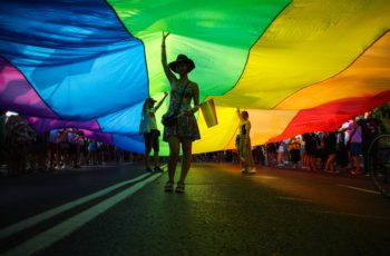 Members of Polish LGBTQ community are seen walking under a giant rainbow flag during the march.