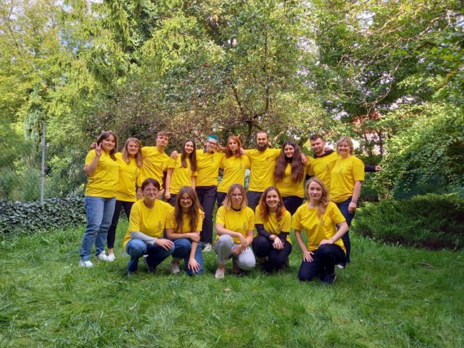 Szkolenie edukatorskie Amnesty International. Grupa uczestniczek_ków pozuje do zdjęcia ubrana w żółte koszulki z logiem Amnesty International, w ogrodzie za siedzibą organizacji.
