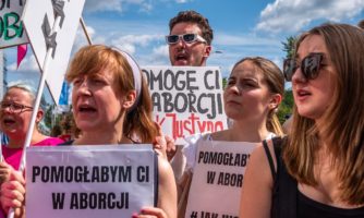 Protest solidarnościowy z Justyną Wydrzyńską pod sądem Warszawa-Praga, 14 lipca 2022. Osoby protestujące trzymają banery z hasłami: "Pomogę Ci w aborcji, jak Justyna"; "Pomogłabym Ci w aborcji".