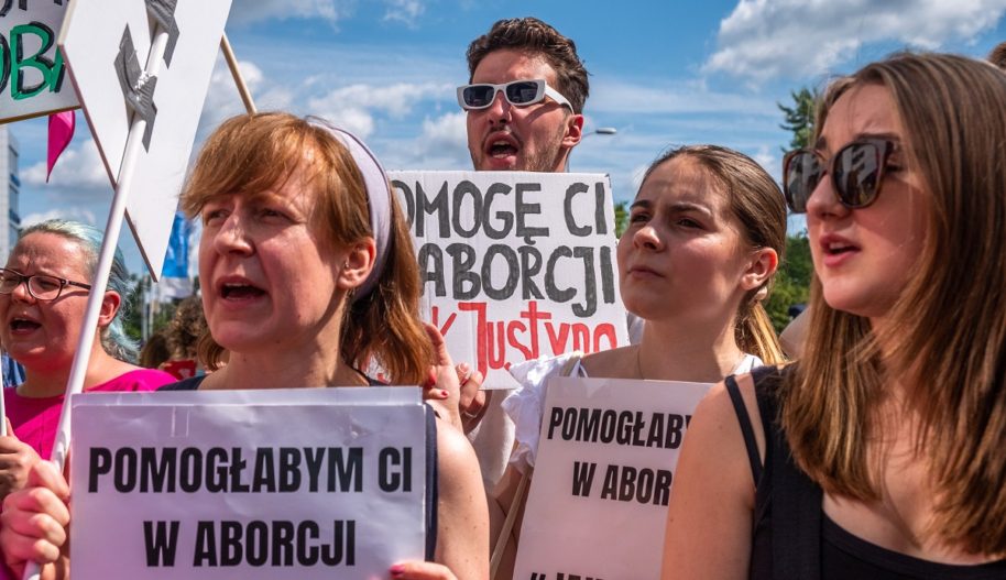 Protest solidarnościowy z Justyną Wydrzyńską pod sądem Warszawa-Praga, 14 lipca 2022. Osoby protestujące trzymają banery z hasłami: "Pomogę Ci w aborcji, jak Justyna"; "Pomogłabym Ci w aborcji".