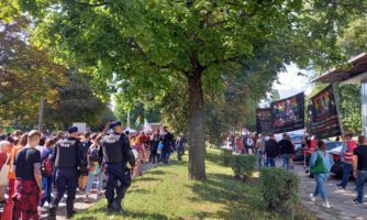 Dwie manifestacje idące ulicą, odgrodzone policjantami, w środku szpaler drzew.