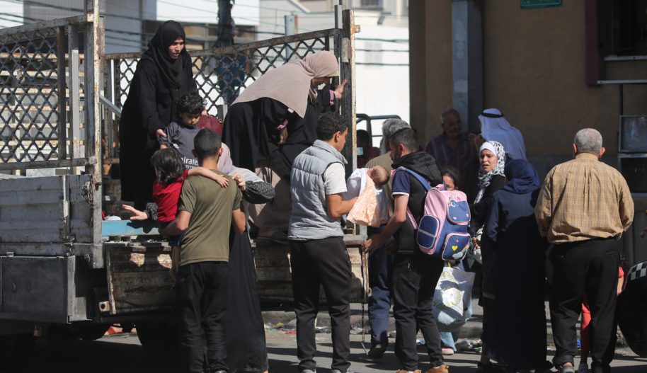Grupa osób uchodźczych przy ciężarówce, wśród nich mężczyźni, kobiety i dzieci.