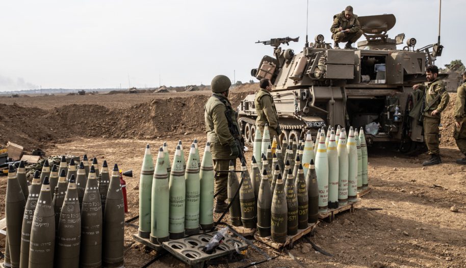 Widok na amunicję wojsk izraelskich, obok kilku żołnierzy, w tle pojazd wojskowy.