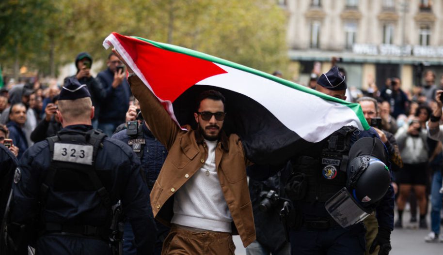 Mężczyzna trzymający flagę Palestyny podczas protestu w Paryżu, obok niego funkcjonariusze policji.