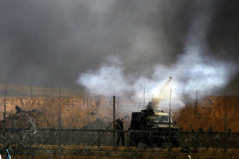 Żołnierz wystrzeliwujący gaz obok pojazdu wojskowego.