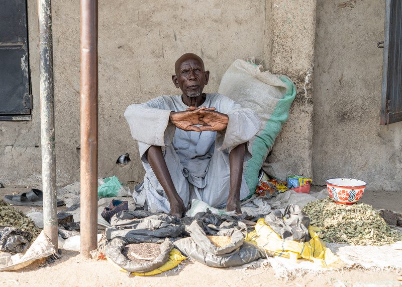 Starszy mężczyzna siedzi, czeka aż uda mu się sprzedać żywność na targu w pobliżu Maiduguri w stanie Borno w północno-wschodniej Nigerii.