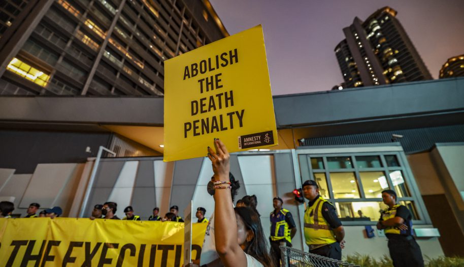 Duża grupa osób protestujących przeciwko egzekucjom, w centrum baner z napisem w języku angielskim nawołujący do zniesienia kary śmierci.