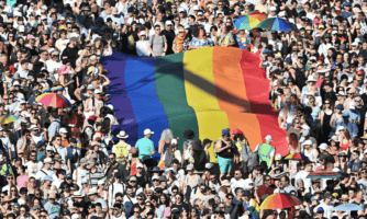 Tłum osób na marszu równości w Budapeszcie, w centrum duża tęczowa flaga.