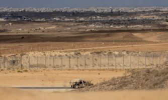 Pojazd wojskowy jadący wzdłuż zasieków, w tle zniszczone budynki w Gazie.