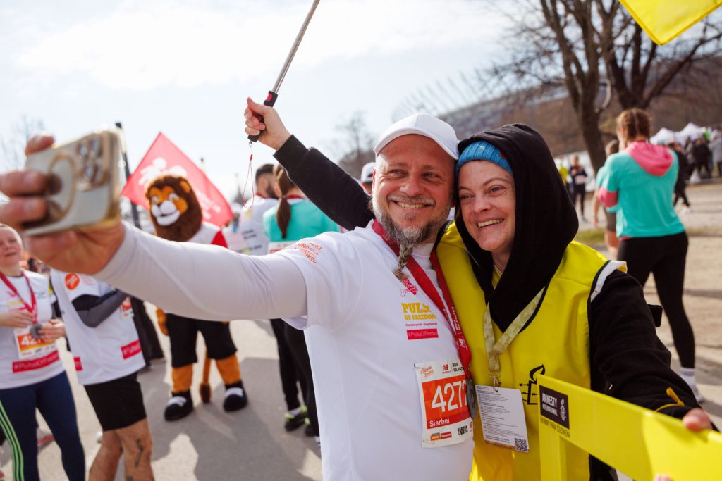 Dwie osoby w strojach do biegania robiące sobie selfie, w tle flaga Amnesty.