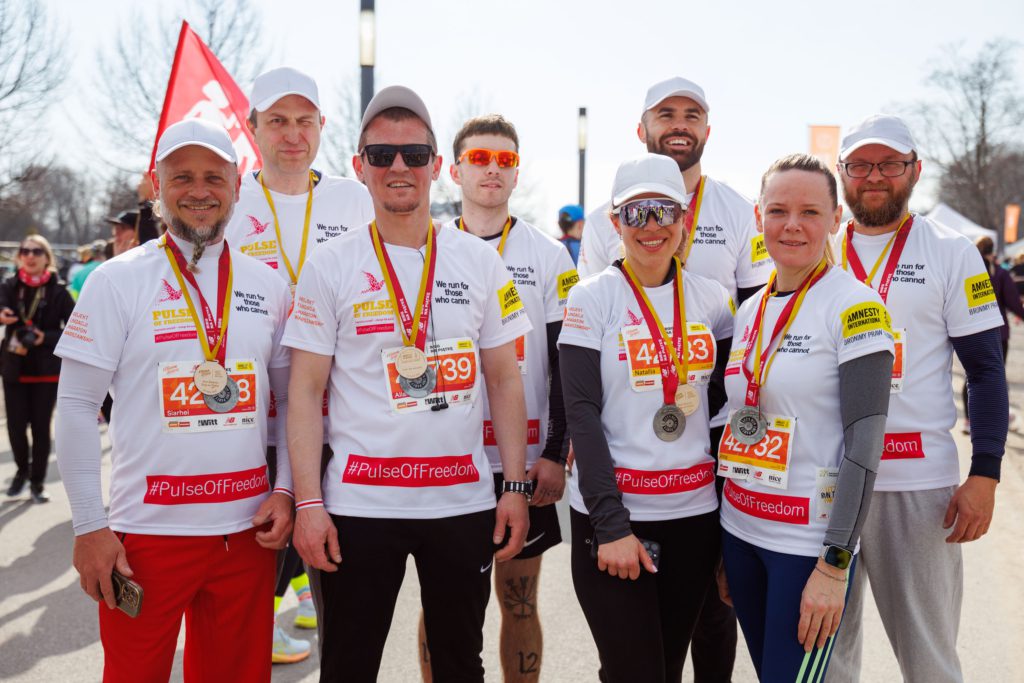 Grupa osób w białych koszulkach biegowych z medalami na szyjach.