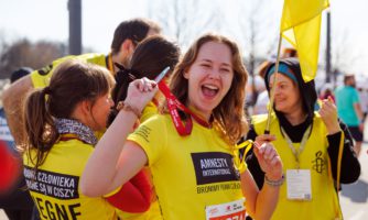 Grupa osób w koszulkach biegowych, na pierwszym planie roześmiana młoda kobieta z medalem.