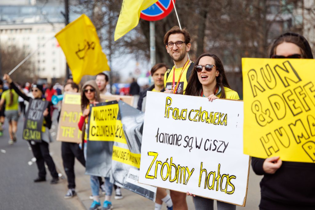 Osoby kibicujące biegaczom przy trasie. Trzymają kolorowe banery.