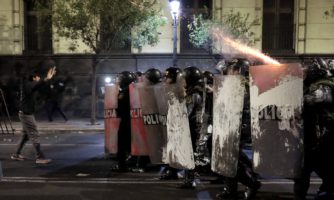 Mężczyzna stojący naprzeciw grupy uzbrojonych policjantów.