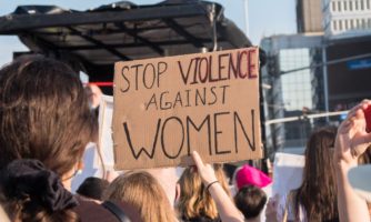 Grupa ludzi na ulicy, osoba w środku trzyma transparent z napisem Stop violence against women