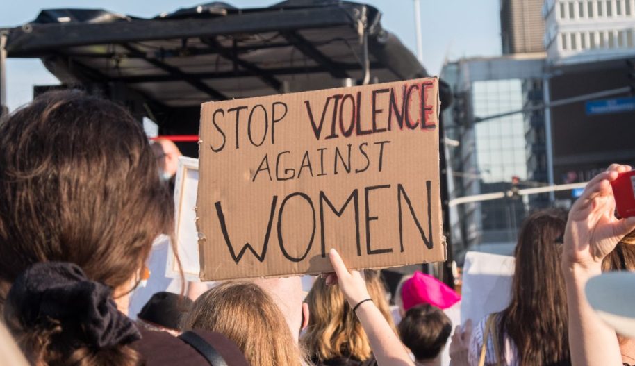 Grupa ludzi na ulicy, osoba w środku trzyma transparent z napisem Stop violence against women